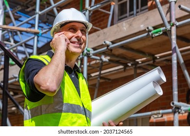 Male builder foreman, worker or architect on construction site, happy, smiling, holding building plans and talking on his cell phone