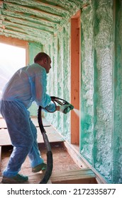 Male Builder Insulating Wooden Frame House. Man Worker Spraying Polyurethane Foam Inside Of Future Cottage, Using Plural Component Gun. Construction And Insulation Concept.