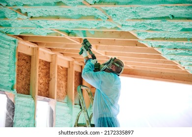 Male Builder Insulating Wooden Frame House. Man Worker Spraying Polyurethane Foam Inside Of Future Cottage, Using Plural Component Gun. Construction And Insulation Concept.