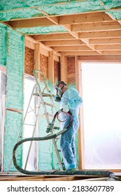 Male Builder Insulating Wooden Frame House. Man Worker Spraying Polyurethane Foam Inside Of Future Cottage, Using Plural Component Gun. Construction And Insulation Concept.