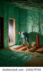 Male Builder Insulating Wooden Frame House. Man Worker Spraying Polyurethane Foam Inside Of Future Cottage, Using Plural Component Gun. Construction And Insulation Concept.