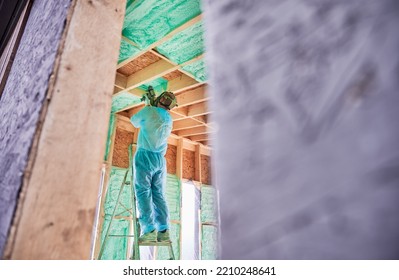 Male Builder Insulating Wooden Frame House. Man Worker Spraying Polyurethane Foam Inside Of Future Cottage, Using Plural Component Gun. Construction And Insulation Concept.