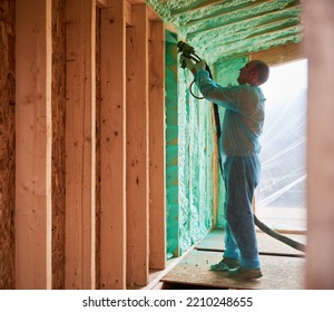 Male Builder Insulating Wooden Frame House. Man Worker Spraying Polyurethane Foam Inside Of Future Cottage, Using Plural Component Gun. Construction And Insulation Concept.