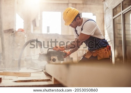 Male builder using wood cutting circular saw machine in workshop