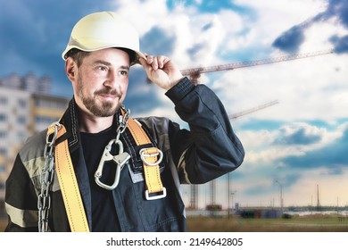 A Male Builder In A White Hard Hat Against A Blurred Background Of A Construction Site With A Blue Sky. Positive Civil Engineer With A Beard