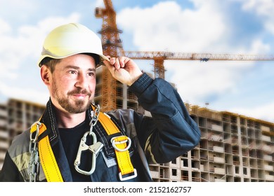 A Male Builder In A White Hard Hat Against A Blurred Background Of A Construction Site With A Blue Sky. Positive Civil Engineer With A Beard