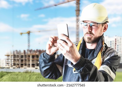 A Male Builder In A White Hard Hat Against A Blurred Background Of A Construction Site With A Blue Sky. Positive Civil Engineer With A Beard