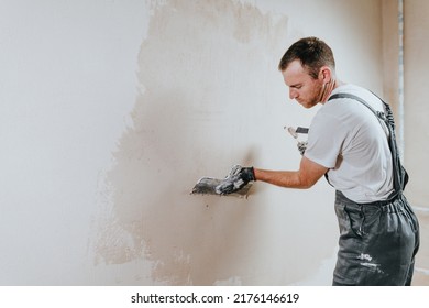 Male builder in work overalls plastering a wall using a construction trowel. Horizontal panorama banner with blank space for text. - Shutterstock ID 2176146619
