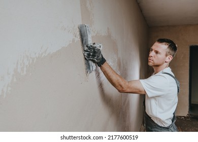 Male builder in work overalls plastering a wall using a construction trowel. Horizontal panorama banner with blank space for text. - Shutterstock ID 2177600519
