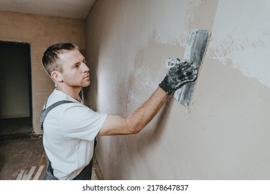Male builder in work overalls plastering a wall using a construction trowel. Horizontal panorama banner with blank space for text. - Shutterstock ID 2178647837