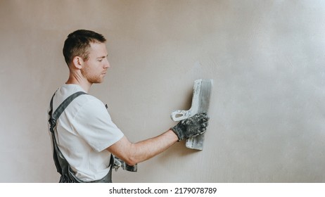 Male builder in work overalls plastering a wall using a construction trowel. Horizontal panorama banner with blank space for text. - Shutterstock ID 2179078789