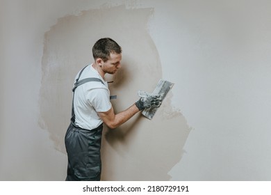 Male builder in work overalls plastering a wall using a construction trowel. Horizontal panorama banner with blank space for text. - Shutterstock ID 2180729191