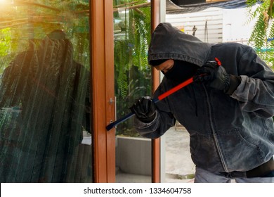 Male Burglar Wearing A Hoodie Forcing Entry Into A House With Crowbar Through A Front Door