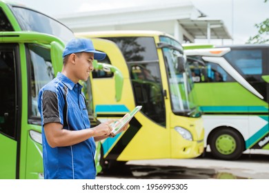 A Male Bus Crew Member In Uniform And A Hat Smiles While Using A Digital Tablet Against The Backdrop Of The Bus Fleet