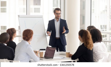 Male business coach speaker in suit give flipchart presentation  speaker presenter consulting training persuading employees client group  mentor leader explain graph strategy at team meeting workshop