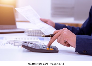 A male business man sits a long time earning money from doing business using a calculator for long words.