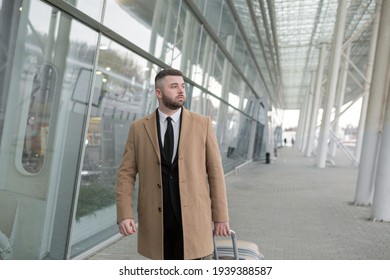 Male businessman, with a beard, in a black jacket and coat, on the background of a large modern business center made of glass