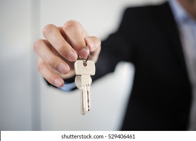 Male Businessman In Black Suit Holding, Giving House Keys, Close-up Of Hand, Indoor