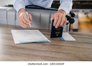 Male Businessman Signing A Travel Health Insurance Form Before A Flight, US Citizen Passport In Hand