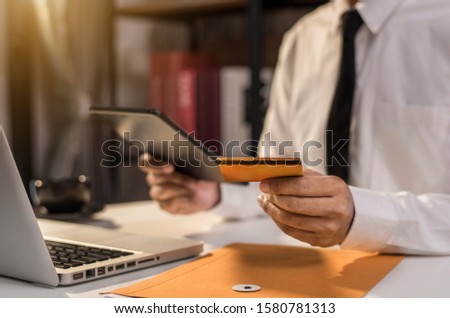 Male businessman use credit cards to conduct financial transactions through phones, tablet, and laptop.