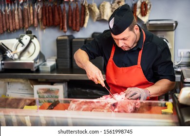 Male butcher boning fresh ham in a modern butcher shop with metal safety mesh glove