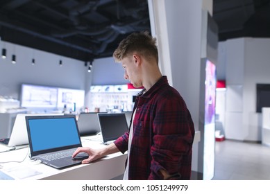 A Male Buyer Looks At Laptops In The Computer Department Of The Electronics Store. The Buyer Chooses A Laptop In A Modern Technology Store