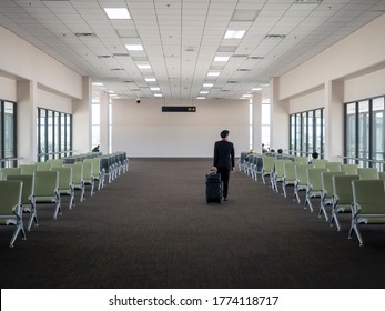 Male Cabin Crew In Black Uniform And Medical Mask Waking With Trolley Bag In Empty Terminal. Airport Terminal With No Or Few Passenger During Covid19.