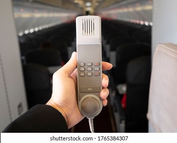 Male Cabin Crew Holding Interphone In Aircraft Cabin. Cabin Intercom For Crew Use.