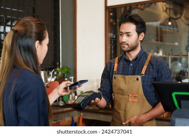 Male cafe employees of various nationalities holding  credit card acceptor and showing  QR code smiled. to  female Asian customer with brown hair holding mobile phone to scan and pay small business. - Powered by Shutterstock