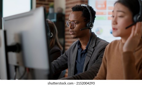 Male call center operator using headset to help people, giving telemarketing assistance to clients on helpline. Person working at customer support service office, offering advice.