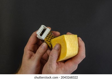 Male calloused hands hold a piece of cheese and grate against a dark gray background. A fermented dairy product high in protein, milk fat, calcium and phosphorus. Useful ready-to-eat food.