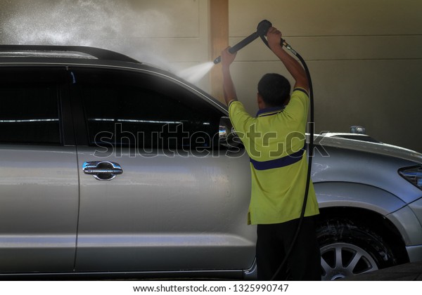 Male car care staff cleaning and washing a\
car by high pressure washer machine with foggy from splashing water\
and sun lighting\
background.