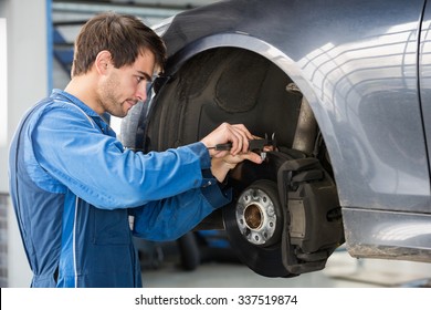 Male car mechanic examining brake disc with caliper in garage