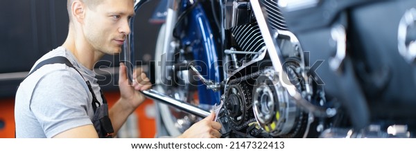 Male car mechanic holds wrench and looks at open\
motorcycle engine