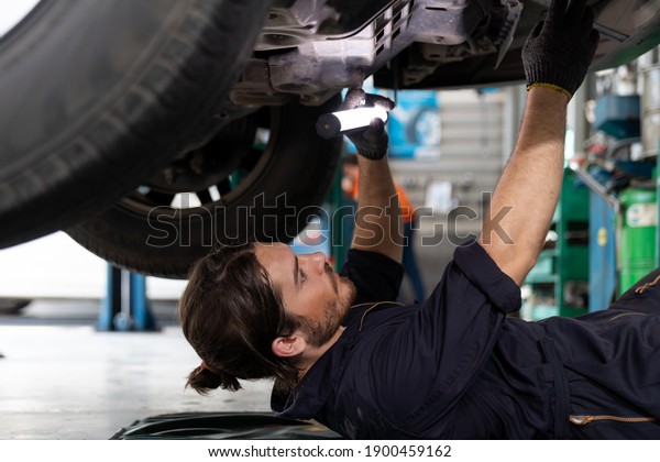 Male car mechanic worker working using wrench\
tool for repair, maintenance underneath lifted car. Mechanic\
vehicle service checking under car in garage. Auto car repair\
service, maintenance\
concept