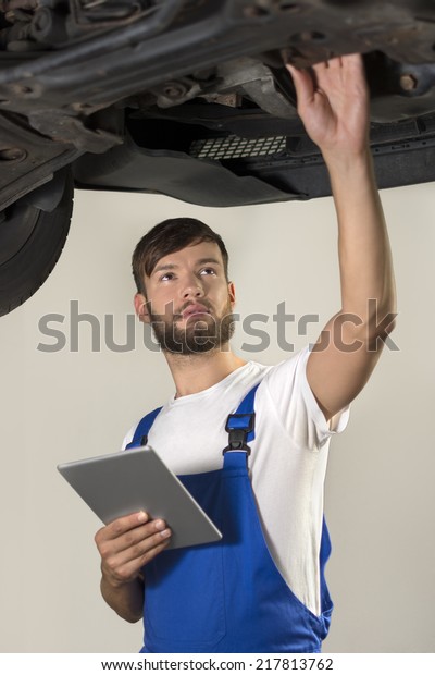 Male car mechanic working under car with tablet PC,\
Studio Shot