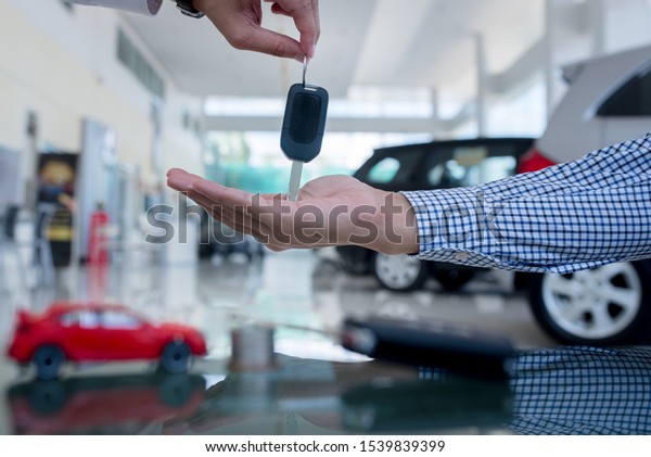 Male car salesman is going to\
give a new car key to an Asian business customer and sign a car\
dealer contract to buy a new car loan, trade money or\
investment.