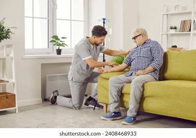 Male caregiver setting up iv drip to senior patient. Senior man sitting on sofa receiving intravenous treatment or vitamin therapy at home. Elderly healthcare, medical care, support - Powered by Shutterstock