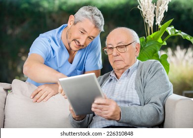 Male caretaker assisting senior man in using digital tablet at nursing home porch