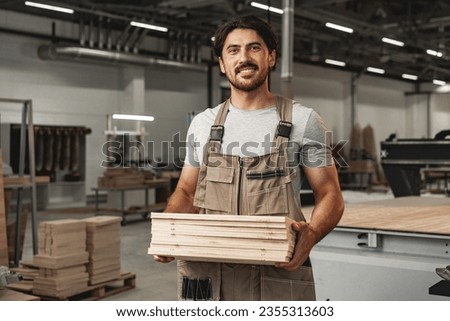 Male carpenter holding wooden planks in workshop
