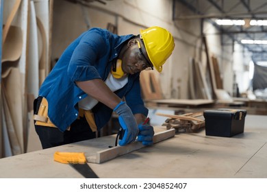 Male carpenter measure the size of wood during working in wood workshop. Male joiner wearing safety uniform, gloves, helmet and working in furniture workshop - Shutterstock ID 2304852407
