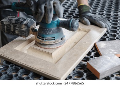 A male carpenter sands wooden furniture facades with a sanding machine at a furniture production factory, wood processing concept - Powered by Shutterstock