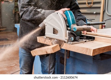 Male carpenter sawing a board with a circular saw in a carpentry workshop close-up