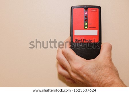Male carpenter using electronic stud finder to locate interior wall stud.