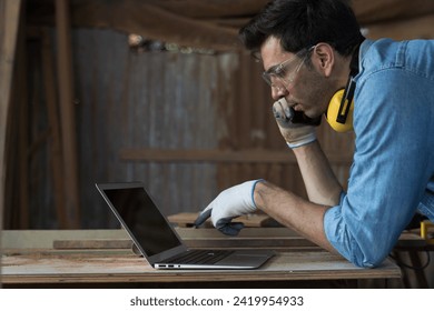 Male carpenter using laptop computer at woodwork workshop. Male joiner working with laptop computer furniture workshop. Start up and small business concept - Powered by Shutterstock