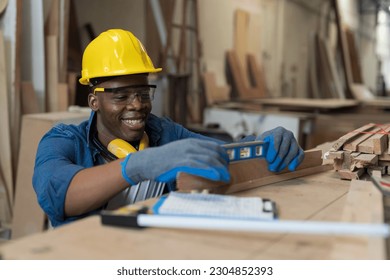Male carpenter using water level measure during working in wood workshop. Male joiner wearing safety uniform, gloves, helmet and working in furniture workshop - Shutterstock ID 2304852393