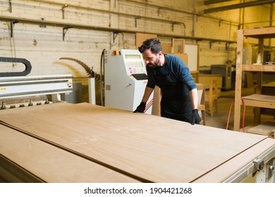Male carpenter working with a plywood sheet in a big workshop. Handsome worker getting ready to cut a wood panel in a woodshop