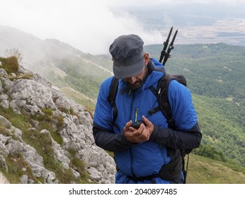 A Male Caucasian Backpacker In Blue Rain Jacket Looking At His Hikking Gadget