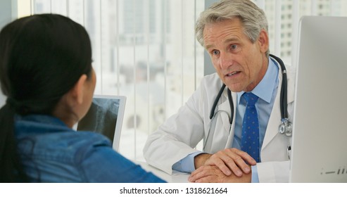 Male Caucasian Doctor Talking To Female Patient About Neck Injury With X-ray On Screen. Woman Listening To Her Health Care Provider Explain Spinal Treatment