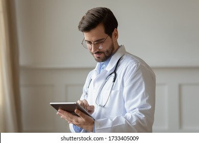 Male Caucasian doctor in white medical uniform fill patient medical history or anamnesis on tablet in hospital, man GP or physician consult client online on pad in modern clinic, healthcare concept - Powered by Shutterstock